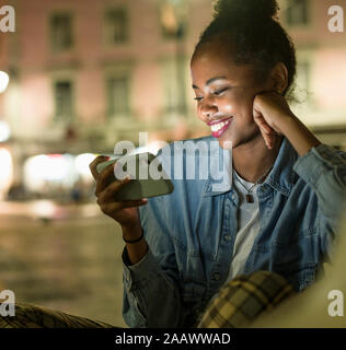 Ritratto di felice giovane donna guardando smartphone di notte, Lisbona, Portogallo Foto Stock