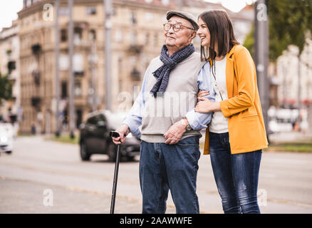 Nipote di adulto assistere suo nonno passeggiando con bastone Foto Stock