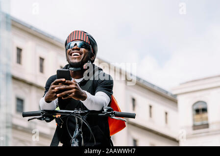 Felice elegante giovane con bicicletta, smartphone e messenger bag in città Foto Stock