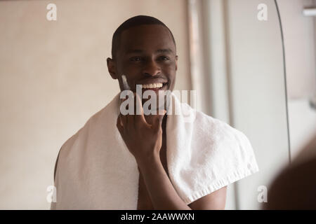 African American uomo applicare la crema per il viso in cerca dello specchio Foto Stock