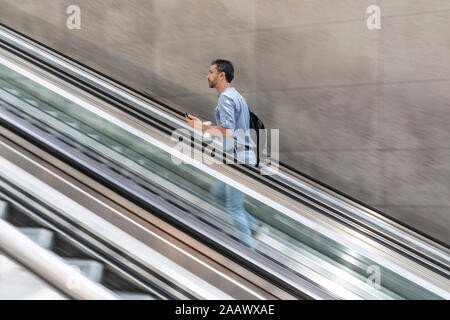 Uomo d'affari che salice la scala mobile in città, Berlino, Germania Foto Stock