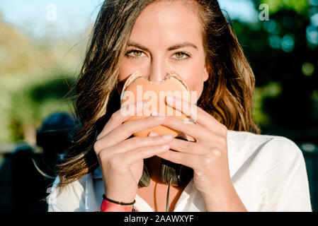 Giovane donna che copre la faccia con un hamburger Foto Stock