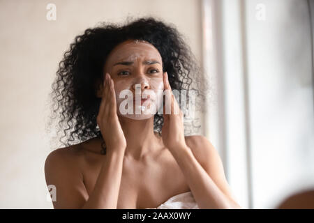 African American donna applicare la crema per il viso in bagno Foto Stock