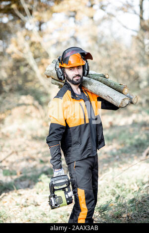 Ritratto di un professionista lumberman in indumenti da lavoro protettiva con un chainsaw e tronchi di legno durante il lavoro sul disboscamento in pineta Foto Stock