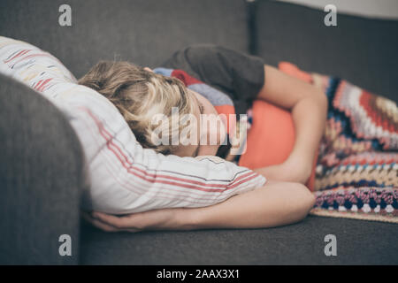 Ragazzo malato a letto con coperta di lana e bottiglie di acqua calda. Triste teen con l'influenza si appoggia a casa da solo in una fredda giornata invernale. Bambino con infettare stagionali Foto Stock