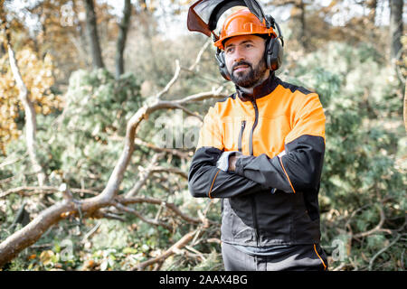 Vita-up verticale di un professionista lumberman in harhat e indumenti da lavoro protettiva in piedi nella foresta di pini Foto Stock