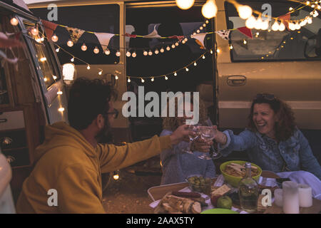 Happy amici tifo e bere il vino durante la vacanza in campeggio in spiaggia con van vintage. Le persone aventi il divertimento a fine settimana serata estiva con campe Foto Stock