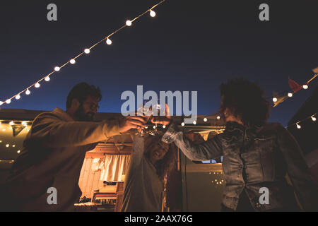 Happy amici tifo e bere il vino durante la vacanza in campeggio in spiaggia con van vintage. Le persone aventi il divertimento a arancione tramonto sotto la mezza luna. Yo Foto Stock