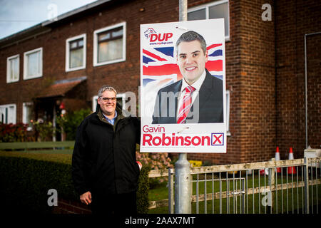 Si prega di tenere premuto fino alle 11.00 di domenica 24 novembre gli operatori storici di Gavin Robinson chi è la partizione DUP candidati per la prossima elezione generale su dicembre XII per la circoscrizione di east Belfast sorge accanto a uno dei suoi vecchi manifesti elettorali mentre adoperando sul Cregagh estate in oriente Belfast. Foto Stock