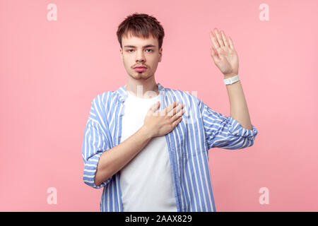 Lo giuro! Ritratto di onesto gravi i capelli castani uomo con piccola barba e baffi in casual striped shirt mantenendo la mano sul petto e rendendo promessa oa Foto Stock