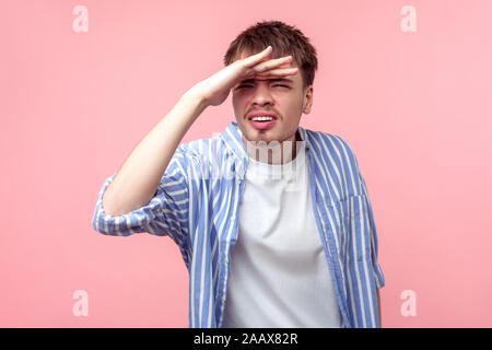 Ritratto di curiosi i capelli castani uomo con piccola barba e baffi in camicia casual guardando lontano con la mano sopra la testa, fissando con sguardo curioso Foto Stock