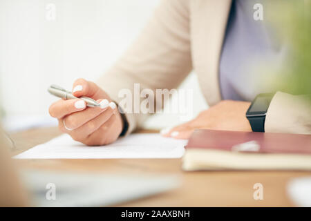 Close up di un irriconoscibile imprenditrice firma documento mentre si lavora alla scrivania in ufficio, concentrarsi sulla mano femmina tenendo pen, spazio di copia Foto Stock