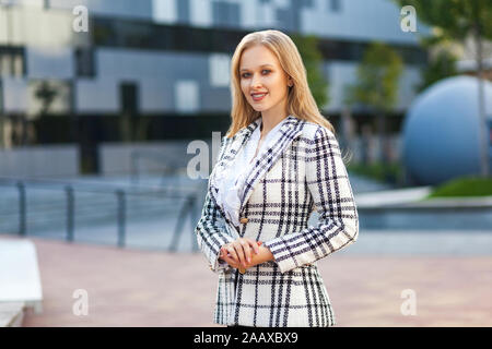 Ritratto della splendida elegante businesslady successo con capelli biondi in plaid camicia fiducioso permanente determinata, tenendo le sue mani insieme, lookin Foto Stock