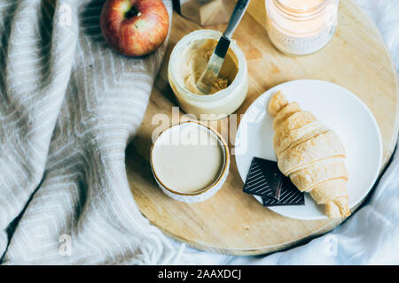 Accogliente winter weekend Colazione, caffè e croissant sul vassoio in legno a letto, filtro vintage Foto Stock