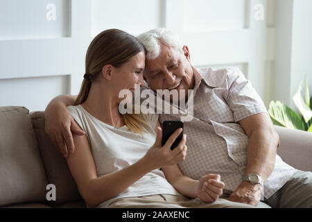 Felice giovane donna che mostra foto divertenti su smartphone al padre. Foto Stock