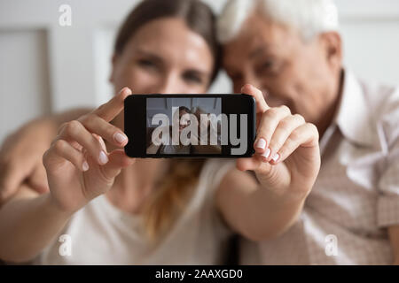 Donna sorridente prendendo foto sul telefono cellulare con padre felice. Foto Stock