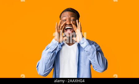 Emozionato Afro ragazzo gridando in piedi sopra arancione di sfondo per studio, Panorama Foto Stock