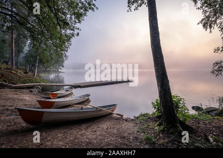 Una bellezza tranquilla mattina con barca a remi e pier al misty estate sunrise in spiaggia idilliaca della Finlandia Foto Stock