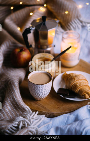 Accogliente winter weekend Colazione, caffè e croissant sul vassoio in legno a letto, filtro vintage Foto Stock