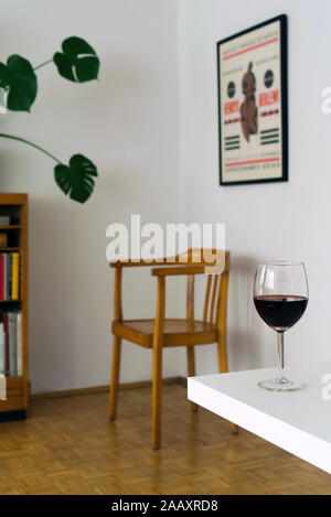 Home interno con un bicchiere di vino rosso sul tavolo bianco, sfocare lo sfondo con la sedia in legno nella camera corner Foto Stock