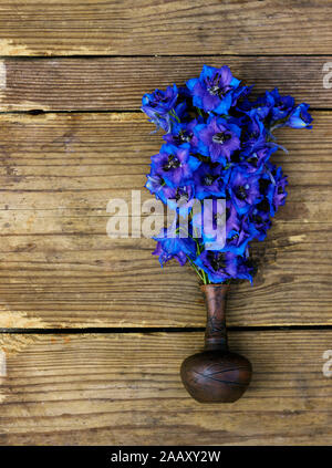 Bouquet di molto luminoso e colorato delphinium blu fiori in un piccolo vaso di creta sul legno rustico squallido sfondo usurati, piatto di laici che, vista dall'alto, clo Foto Stock