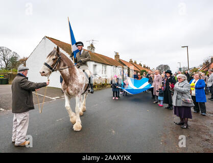 Athelstaneford, East Lothian, Scozia, Regno Unito. Il 24 novembre 2019. Si intraversa Festival: il primo giorno del festival annuale di mark St Andrew's Day avviene nel luogo di nascita della Scottish bandiera nazionale dove la si intraversa apparve nel cielo come un buon auspicio quando il Picts & scozzesi hanno sconfitto i sassoni guidati da Athelstan. Nella foto: Craig Donnelly su una fragola Stefano Clydesdale mare con lo sposo/proprietario Arthur Greenan con gli abitanti dei villaggi compresi i bambini sfilano lungo la strada principale che porta un gigante si intraversa bandiera Foto Stock