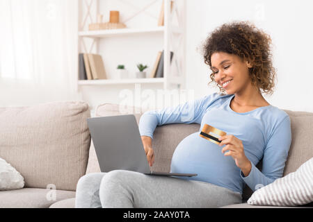 Gravidanza africana Madre ordinazione di vestiti per il suo bambino, utilizzando laptop Foto Stock