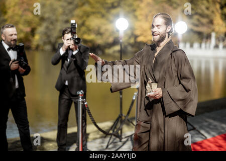 Uomo in costume come un ben noto personaggio del film a piedi con fastidiose foto Reporters sul tappeto rosso durante la cerimonia di premiazione Foto Stock