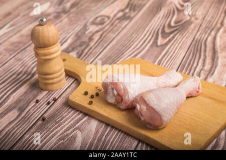 Materie le cosce di pollo su un tagliere e pepe in grani di pepe con mulino. Sul tavolo di legno Foto Stock