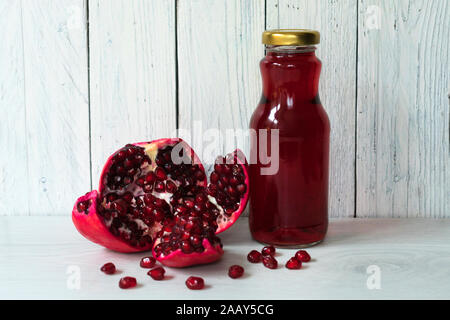 Il Melograno e una bottiglia di succo di melograno su un bianco sullo sfondo di legno. Foto Stock