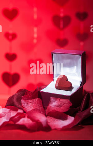 Valentines amore del cuore. Una romantica confezione regalo circondato da petali di rosa e altri simboli di amore e il giorno di San Valentino. Foto Stock