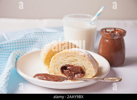 Cornetti freschi bun con cioccolato sulla piastra, una tazza di caffè, un vasetto di latte nelle vicinanze sullo sfondo bianco. Foto Stock