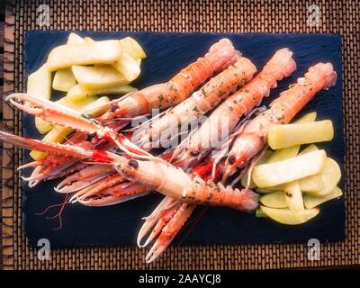 Scampi con prezzemolo e patate fritte su una piastra di ardesia Foto Stock