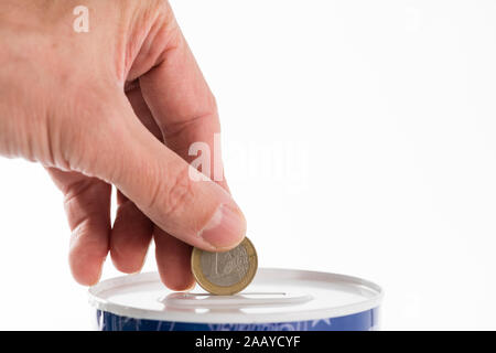 Maschio mettendo mano una moneta da un euro in barattolo di latta saving bank su sfondo bianco. Foto Stock