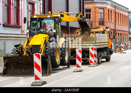 Un escavatore scava un solco sulla strada e si versa la massa in un carrello Foto Stock