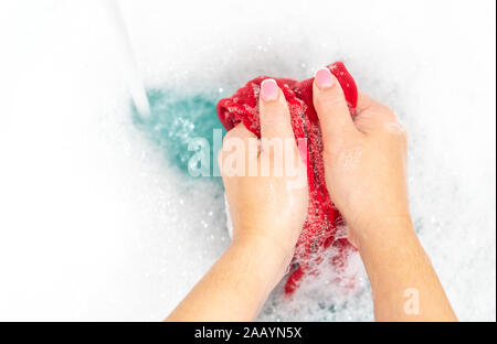 Mani femminili il lavaggio di vestiti di colore nel bacino Foto Stock