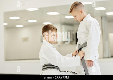 Ragazzo tieing la cinghia sul kimono attorno a un suo amico in vita e mostra a lui come a farlo prima del training Foto Stock