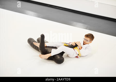 Little Boy in kimono praticando tecniche con il manichino sul pavimento lui imparare a combattere Foto Stock