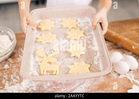 Le mani delle donne tenendo il vassoio con il formato raw i cookie in cucina tavola prima della cottura in forno Foto Stock