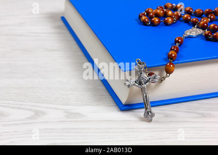 Rosario marrone con chicchi di colore giacente su di un libro su un bianco tavolo in legno Foto Stock