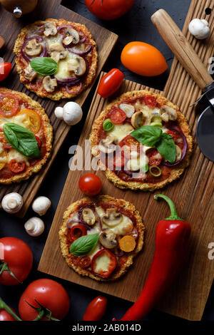 Un sano comfort food o cheto concetto di dieta. Il cavolfiore senza glutine pizze con funghi, melanzane, pomodori e basilico con materie prime on dark b Foto Stock