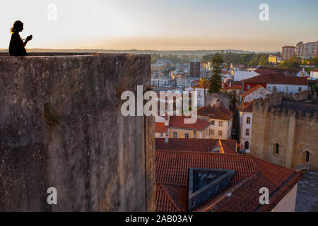 Giovane donna turistica prendendo immagini dal punto di vista uptown al tramonto, Coimbra Città Vecchia, Portogallo Foto Stock