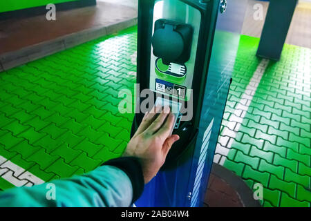 Un uomo paga per la ricarica di un auto elettrica. Mano azienda catd a pagare alla stazione di carica. Concetto di elettricità verde, ambiente pulito, emissione Foto Stock