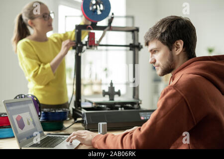 Uomo serio concentrare sul lavoro su nuovi oggetti sullo sfondo del suo collega lo stelo di controllo sulla stampante 3D Foto Stock