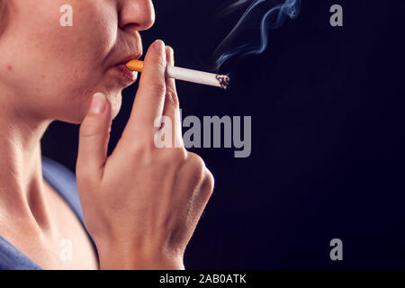 La donna fuma sigaretta su sfondo nero. Il tabagismo concept Foto Stock