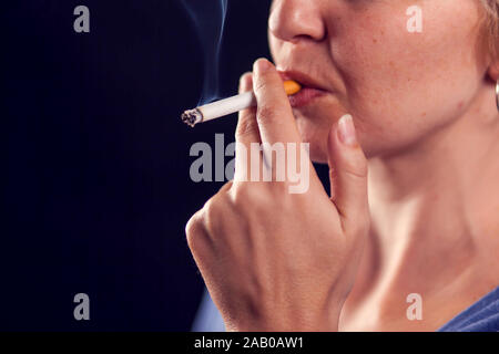 La donna fuma sigaretta su sfondo nero. Il tabagismo concept Foto Stock