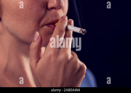 La donna fuma sigaretta su sfondo nero. Il tabagismo concept Foto Stock