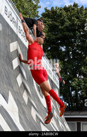 Uomo in abito rosso cercando di conquistare un ostacolo a se Viking race 2019 a Helsinki in Finlandia Foto Stock