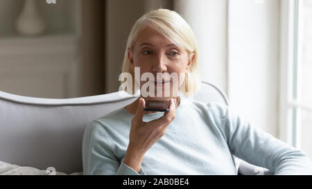 Donna anziana tenendo lo smartphone utilizza virtual Assistente vocale Foto Stock