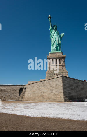 Statua della Libertà, girato a Liberty Island in inverno con la neve e il piedistallo visibile. Girato in luce diurna soleggiata con cielo blu chiaro. Foto Stock